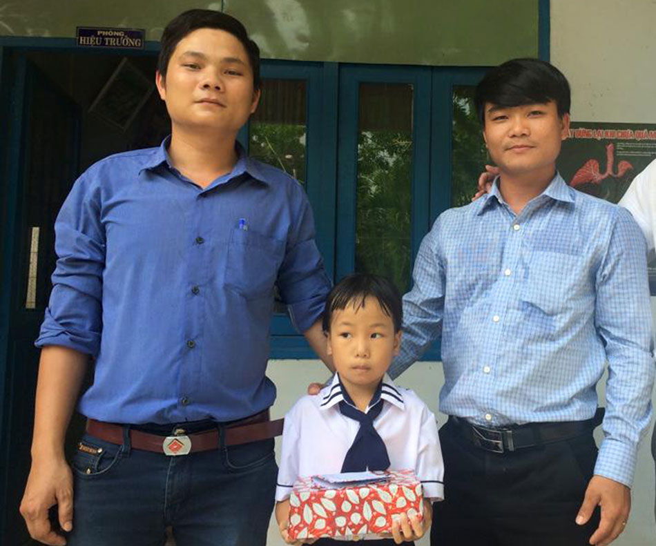 Nguyễn Công Toản (bìa phải) trao quà cho một học sinh nghèo ở xã Hòa Tân Đông.